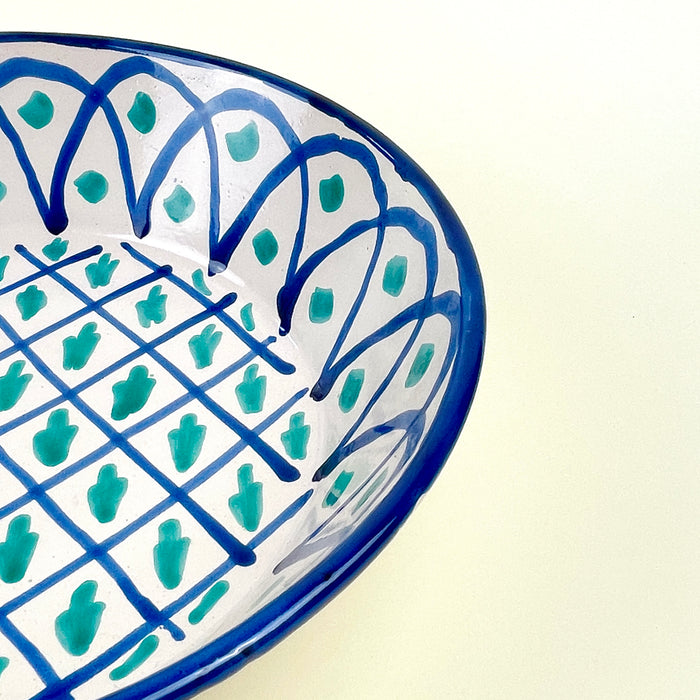 Large Granada lebrillo bowl in hand painted ceramic, made with a cream glazed ground, blue lattice decoration, green motifs, and a repeated arched border around the inner wall. The bowl can be displayed upright using the pierced hanging hole or styled flat as a table centerpiece for Mediterranean decor and Spanish farmhouse decor.