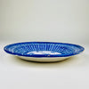 Signed Manises ceramic wall plate from early 20th century Spain, decorated by hand with saturated cobalt blue brushwork on a warm white glazed ground. Intersecting lines form a basket weave pattern around the rim, while the central medallion contains a plant sprig, leaf-like marks, and small crosshatched symbols suited to blue and white decor.
