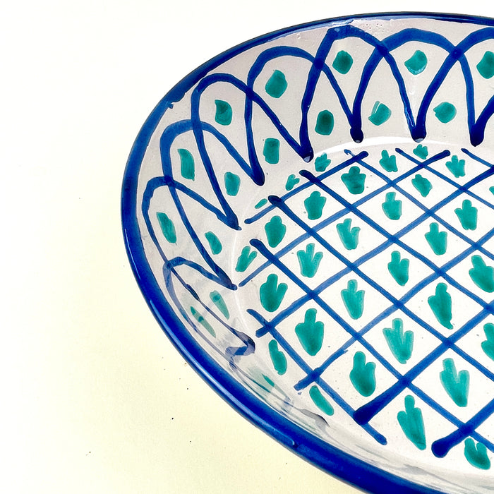 Spanish lebrillo bowl with pierced hanging hole, exposed terracotta clay edge, glossy white glaze, and bold green blue Fajalauza decoration. The deep rounded form suits wall display, fruit or bread presentation, farmhouse decor, Mediterranean decor, and collected Spanish ceramic interiors with handmade pottery character.