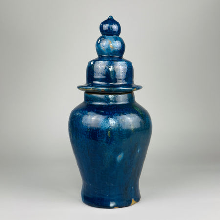 Handcrafted blue ceramic jar with tall tapered form and triple-tiered lid, finished in a mottled deep blue glaze with visible drips and glaze pooling, ideal as a sculptural shelf accent or centerpiece in modern, eclectic, or Mediterranean interiors.