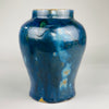 Close-up of blue ceramic surface showing layered glaze effects and irregular textures, including cobalt speckling and greenish drips, emphasizing the handcrafted nature and visual richness of the artisan finish.
