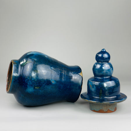 Large artisan ceramic jar photographed front-facing with lid in place, featuring vibrant blue glaze variations and gourd-like finial, perfect for collectors of contemporary pottery or statement interior decor.