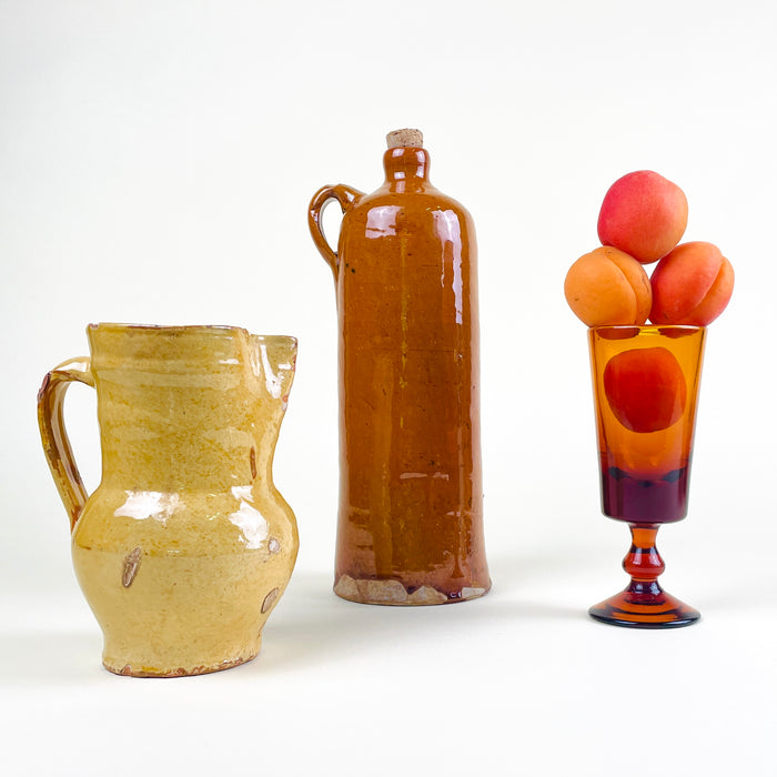 Antique Peñafiel jug in yellow glazed terracotta, representing traditional Castilian folk pottery from Valladolid, Spain. The small earthenware vessel has a practical pitcher form with a rounded belly, tall neck and loop handle, plus extensive surface wear and exposed clay that make its age and handmade construction clearly legible.