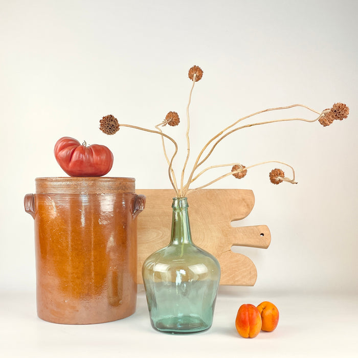 Early 20th-century French stoneware crock identified as a large confit pot with lid, twin pierced handles, and a pale glazed interior. The exterior combines russet, honey, and dark brown tones with age-related surface variation and traces of domestic use. Its authentic utilitarian form works as an antique storage jar, farmhouse centerpiece, or French country decor accent.