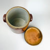 French country decor vessel formed as a large antique confit pot with its fitted lid and heavy stoneware construction. The warm chestnut-brown glaze, pale interior, compact ear handles, and ribbed wheel-thrown details create a restrained farmhouse character. Use this early 20th-century crock as a storage jar, utensil holder, dried flower vase, or sculptural centerpiece.