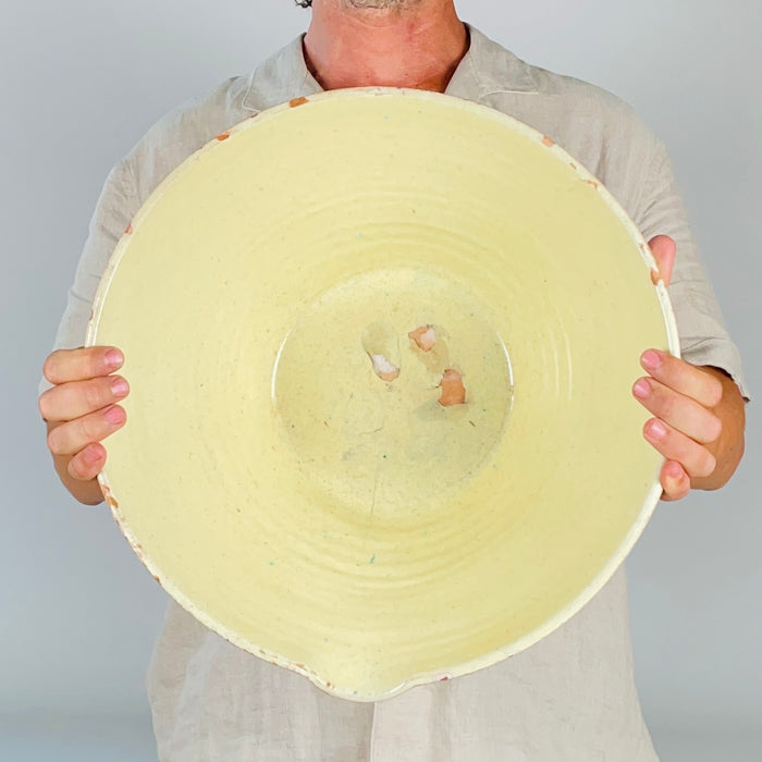 Early 1900s French tian bowl from Provence, showing small chips and glaze losses around the edge where the warm terracotta clay is exposed. The pale yellow interior glaze has fine speckling and natural surface variation, while the worn lip records decades of use and gives this antique pottery authentic farmhouse decor character.