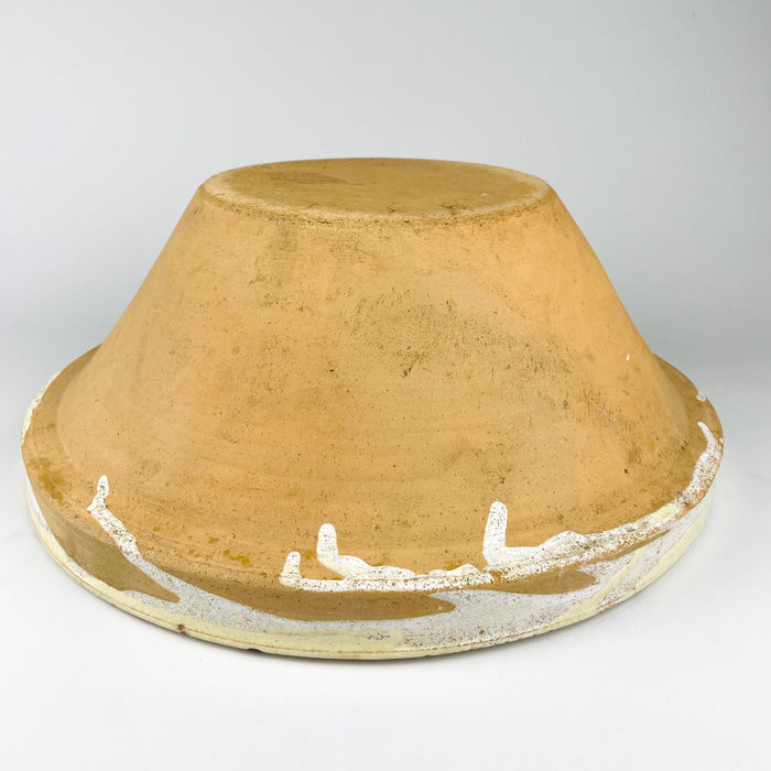 Underside of an antique XL French terracotta tian bowl from Provence, dating to the early 1900s, showing the broad flat base, warm ochre clay body, circular wheel marks, scratches, and darkened age wear. The raw exterior contrasts with the glazed upper rim, reinforcing its authentic provincial pottery character for farmhouse decor and Mediterranean decor.