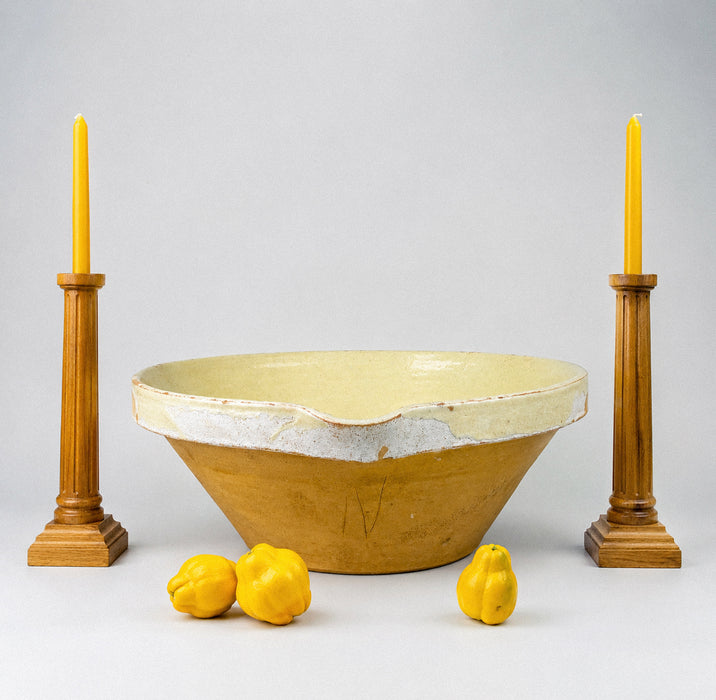 Antique XL French terracotta tian bowl held to demonstrate its substantial scale, with a broad open mouth, deep conical basin, pale cream-yellow glazed interior, and worn rim exposing warm red clay beneath. This Provence pottery piece has the sculptural size and aged surface sought for farmhouse decor, French country decor, and Mediterranean decor.