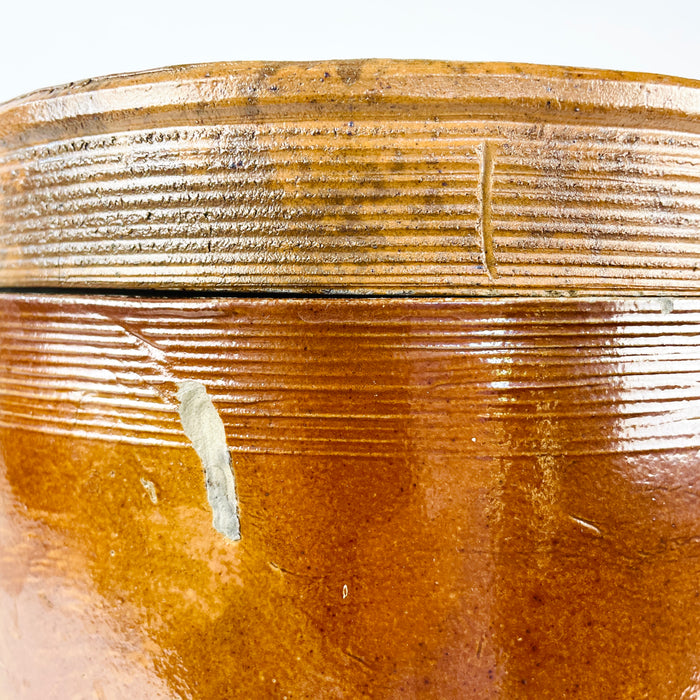 Early 20th-century French provincial confit pot in heavy brown glazed stoneware, complete with a fitted circular lid and two applied handles. Ribbed throwing lines around the lid and shoulder emphasise its handmade construction, while the pale interior glaze supports its original storage function. This antique crock brings aged pottery texture to farmhouse decor, Mediterranean decor, or cottage decor.