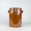Large antique French confit pot with its matching fitted lid, made in early 20th-century stoneware with a warm brown and amber exterior glaze, pale grey-beige glazed interior, cylindrical body, horizontal throwing rings, and two pierced ear handles. This substantial storage jar and stoneware crock suits French country decor, farmhouse decor, or use as a decorative vase for dried branches.