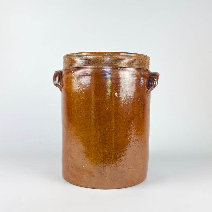 Large antique French confit pot with its matching fitted lid, made in early 20th-century stoneware with a warm brown and amber exterior glaze, pale grey-beige glazed interior, cylindrical body, horizontal throwing rings, and two pierced ear handles. This substantial storage jar and stoneware crock suits French country decor, farmhouse decor, or use as a decorative vase for dried branches.