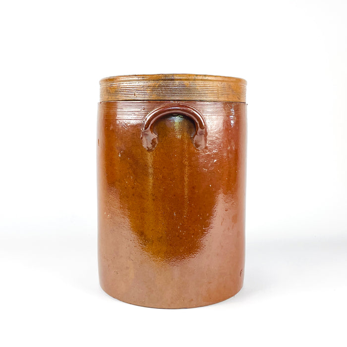 Brown glazed French confit pot dating to the early 20th century, made from dense stoneware with wheel-thrown rings, a broad opening, two pierced ear handles, and its fitted lid. Natural firing variation, minor glaze losses, scratches, and patina document its former household use. This antique crock adds authentic texture to farmhouse decor, wabi sabi decor, and vintage kitchen settings.