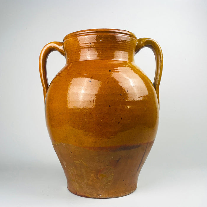 Antique Spanish terracotta storage jar with two handles, XL scale at 39 cm tall and 33 cm wide, wheel thrown earthenware with a warm honey amber glaze across the shoulder and upper body. Natural glaze break and drip lines transition to a more matte terracotta lower half, creating strong Mediterranean decor character.