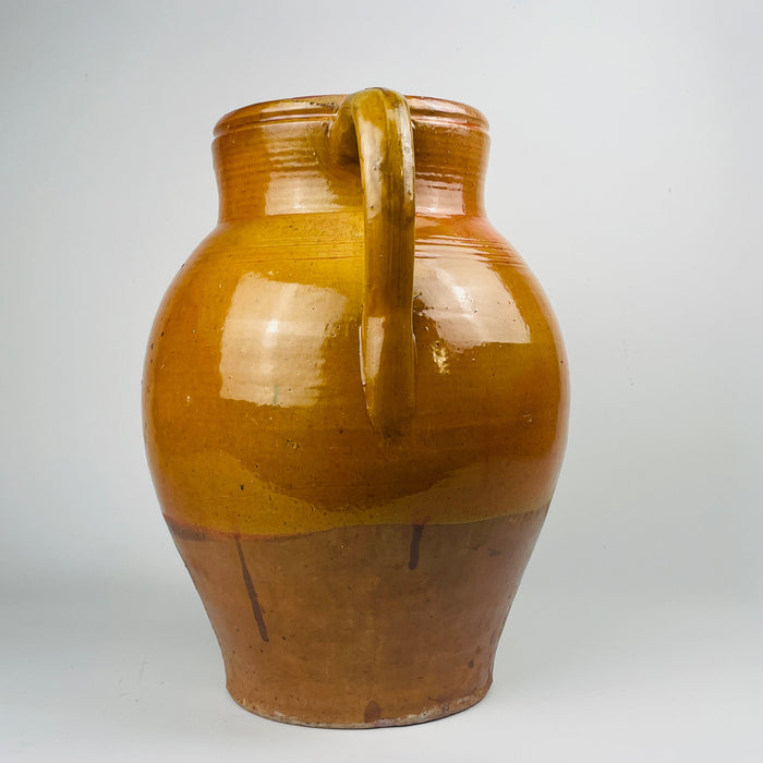 Spanish glazed terracotta olive jar in a two handle form, traditional earthenware vessel with rolled rim and visible throwing rings. The glossy amber glaze shows kiln variation and pooling, while the unglazed terracotta base shows authentic wear and surface rub, ideal for rustic home decor and farmhouse decor styling.
