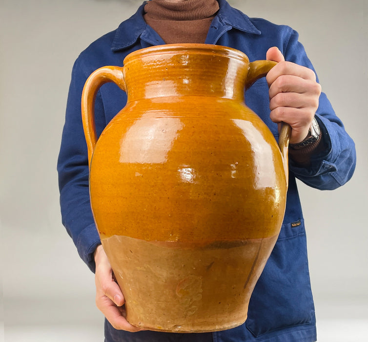 Large Spanish glazed terracotta jar with two handles and a rounded shoulder, hand finished with a honey brown glaze that pools and reflects light. The glaze break creates a band of drip trails over the terracotta lower section, emphasizing traditional pottery techniques and making it suitable for statement floor vase decor.