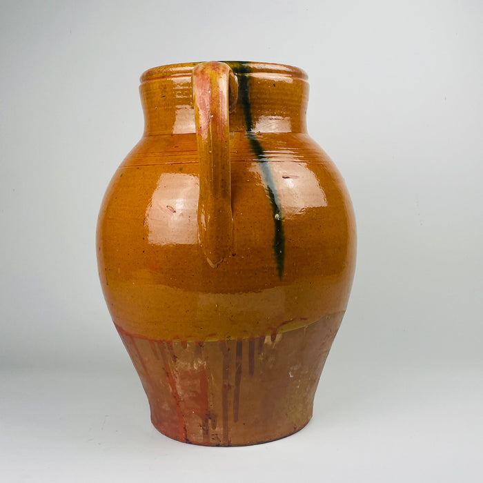 Large antique Spanish terracotta jar with twin handles and a wide mouth, finished in honey brown glaze over terracotta with a clear glaze line and drip trails. The surface patina, firing specks, and handmade form support its use as a floor vase or decorative storage jar in Mediterranean decor interiors.