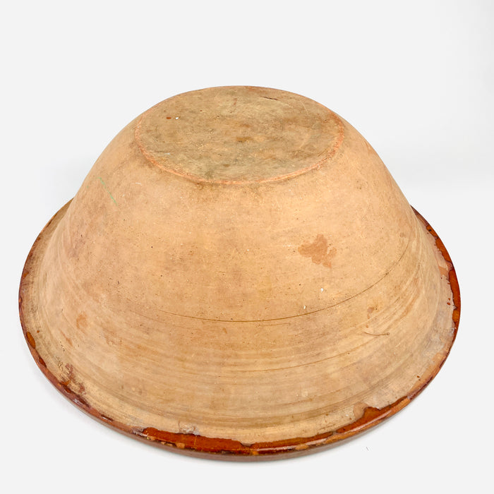 The underside of the antique French tian bowl exposes its unglazed terracotta construction, broad rounded body, circular foot, and wheel thrown ridges. Surface deposits, scratches, clay discoloration, and small edge losses are consistent with long practical use, while the substantial handmade form reinforces its appeal as authentic French country pottery.