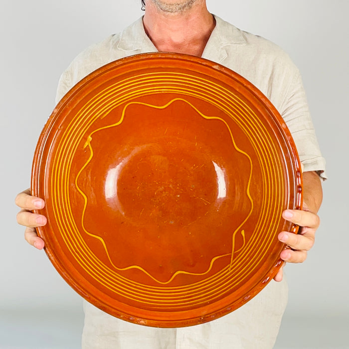 Large antique French tian bowl formed from wheel thrown terracotta, with a warm reddish brown glazed interior and repeated yellow lines following the curve of the bowl. The broad opening, substantial rolled rim, and earthy exterior give this Southern French pottery strong presence as a decorative bowl, fruit bowl, or rustic table centerpiece.