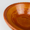 The glazed interior of the antique French tian bowl reveals fine yellow hand applied bands beneath the rim and a loose undulating line surrounding the central well. Warm amber and burnt orange tones, small firing marks, surface scratches, and gentle glaze wear preserve the authentic character of this early 20th century Southern French pottery bowl.