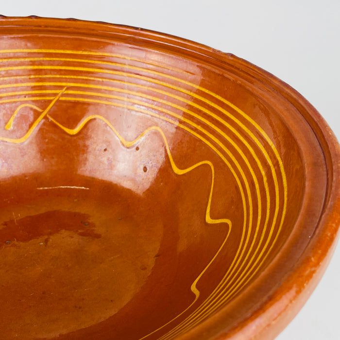 Yellow linear decoration curves across the reddish brown glazed interior of this antique French terracotta bowl, forming parallel rings and a large freehand wavy motif. The visible variation in line width, glaze tone, and surface texture records its handmade character and makes the XL tian a distinctive farmhouse decor or Mediterranean decor centerpiece.