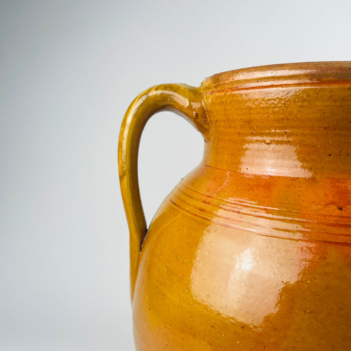 Spanish two handle terracotta olive jar, large decorative vessel with glossy amber glaze and natural drip lines where glaze meets exposed terracotta. The wide mouth and substantial body allow styling as a floor vase for tall branches or as a decorative storage jar, aligning with Mediterranean decor and coastal decor palettes.