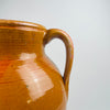 Antique Spanish terracotta storage jar in warm glazed earthenware, showing fine firing speckles and subtle tonal variation across the amber glaze. The lower body transitions to matte terracotta with visible rub and scuffing, creating an authentic aged look that works well in wabi sabi decor and rustic home decor spaces.