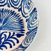 Close-up of rim section showing cobalt spiral wave motif and visible rim chip, illustrating the natural wear and character of this antique Spanish pottery while emphasizing the hand-painted detailing and glaze variation.