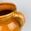 Antique Spanish glazed terracotta jar with a distinctive vertical green glaze run on the shoulder area, adding a one-of-a-kind kiln mark to the amber glaze field. Two handles frame the rounded body, and the terracotta base shows wear consistent with age, making it a strong focal piece for farmhouse decor.