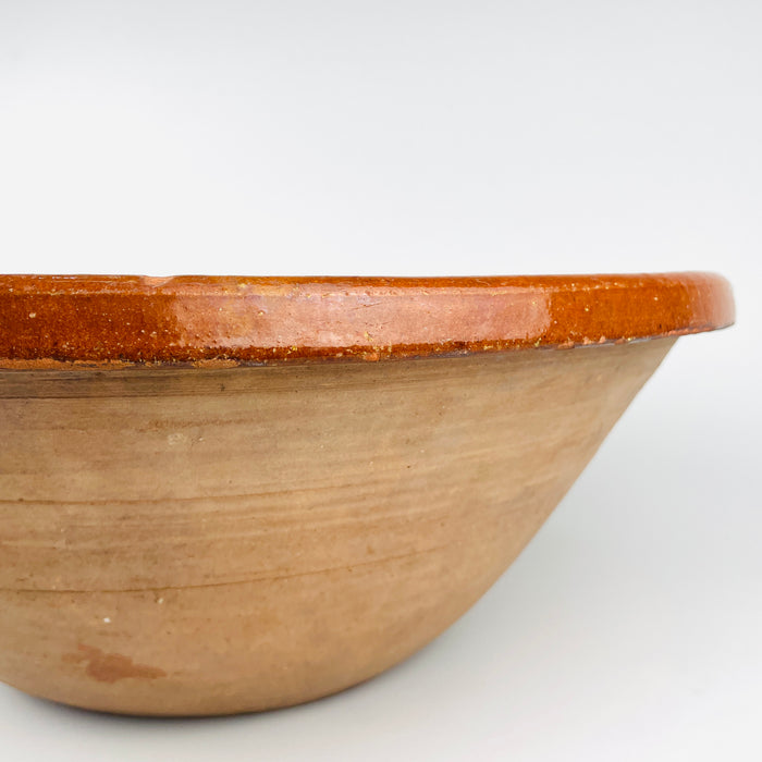 The rolled rim and upper interior of the antique French terracotta tian bowl feature closely spaced yellow lines over a glossy orange brown glaze. Minor rim losses, glaze variation, and the irregular movement of the hand applied decoration emphasize the age and regional craftsmanship of this Southern French pottery piece without diminishing its decorative presence.