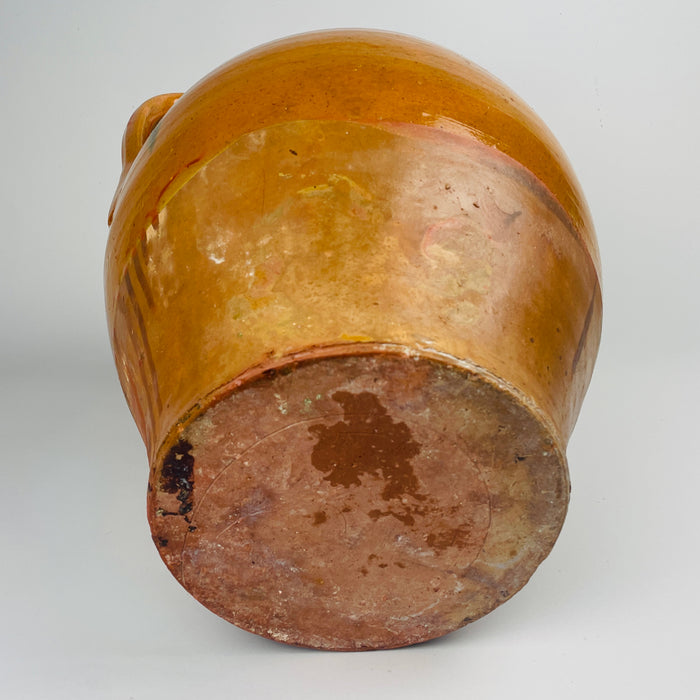 Antique Spanish glazed terracotta jar with two handles, XL scale pottery vessel with honey glaze, drip lines, and visible kiln variation including a green glaze run. The raw terracotta lower body shows age wear and rubbing, while the wide mouth supports styling as a floor vase with dried branches for japandi decor.