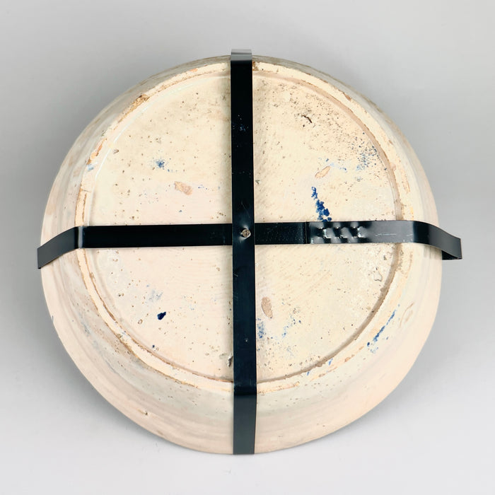 The rear of the ceramic bowl fitted with a cross-shaped black metal wall mount, allowing the 19th-century Fajalauza lebrillo to be displayed vertically as a decorative element in Mediterranean or rustic interiors.