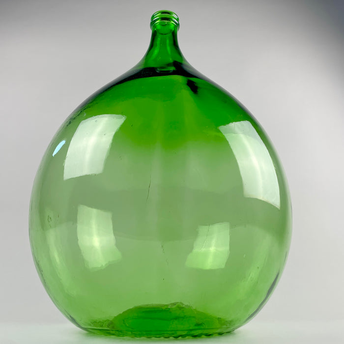 Large French dame jeanne in translucent bottle-green glass, with a rounded 25 L body, elegant tapering shoulders, and a narrow neck above the original utilitarian wine-vessel form. Display this vintage demijohn beside a console or fireplace, or use it with tall branches in French country decor, farmhouse decor, or Mediterranean decor.