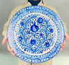 Spanish Fajalauza style platter with a hand painted pomegranate at the center, surrounded by cobalt blue flowers, curling stems, and a dense vegetal border on a white glazed ground. This contemporary ceramic platter can be displayed as a wall hanging plate or used as a large serving charger in Mediterranean decor, Spanish decor, or rustic dining interiors.