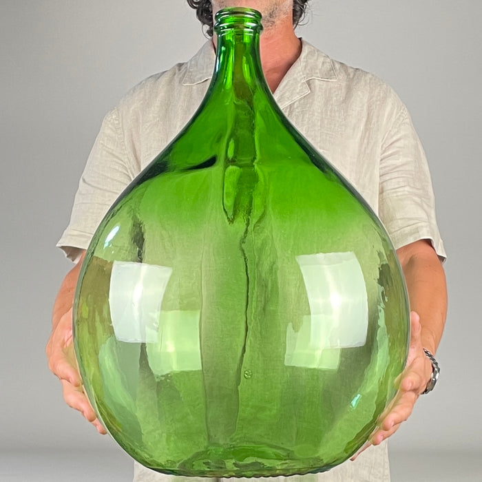 Extra large vintage French green glass demijohn with an estimated 25 L capacity, a deep emerald translucent finish, broad bulbous teardrop body, steep shoulders, narrow neck, and reinforced double-ring mouth. This early to mid 20th century wine carboy works as a sculptural floor vase for French country decor, farmhouse decor, Mediterranean decor, or wabi sabi decor.
