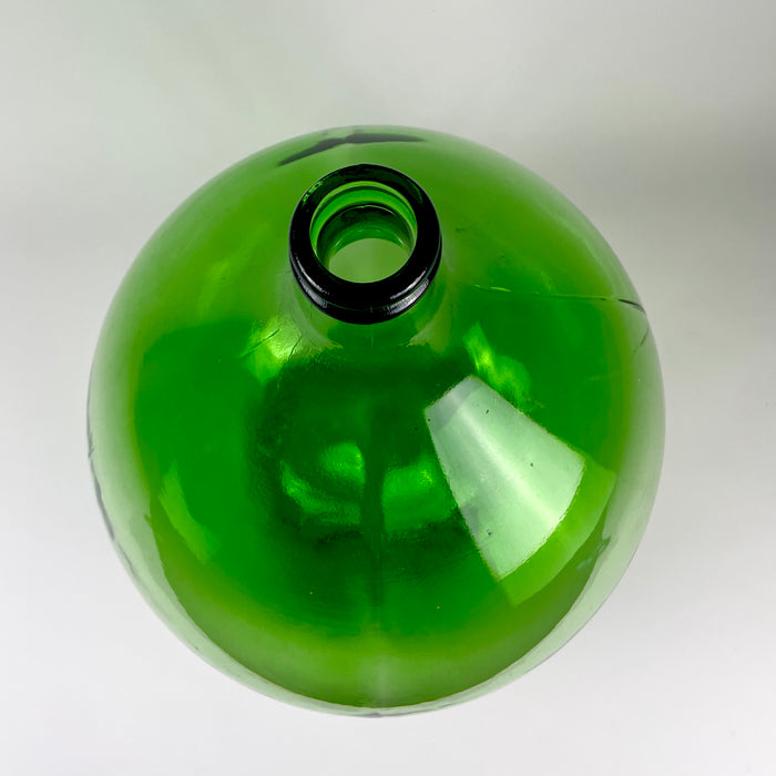 Emerald-green vintage French demijohn with a generous wine carboy form and saturated color that deepens around the shoulders and neck. The rounded glass body shows bubbles, ripples, scratches, and variations in thickness associated with its utilitarian manufacture, adding authentic texture to French country decor or wabi sabi decor.