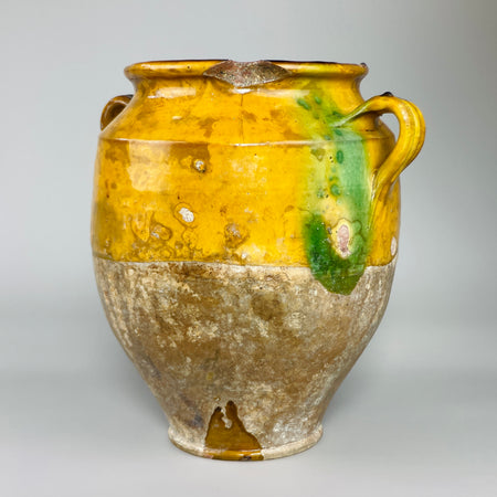 Close-up side view of antique jar’s vibrant yellow glaze and green drip, with a curved ear handle. Aged crackling and glaze loss give this Provençal confit pot visual texture and appeal for use in rustic French country-inspired decor.