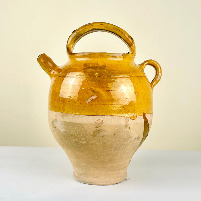 Ceramic jar with a yellowish-brown glaze. Antique French gargolette pottery jug from the 19th century featuring a rich yellow glaze over unglazed terracotta. Includes arched handle, side grip, and original lid, reflecting rural Figeac pottery tradition. Perfect for farmhouse decor, rustic home styling, and Mediterranean interiors.