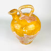 Early 19th-century French gargoulette photographed in profile to emphasize its full rounded body, high loop handle and exceptionally broad pinched spout. Mustard-yellow glaze survives across the shoulder and upper body, contrasting with exposed terracotta and accumulated mineral wear from prolonged household use.