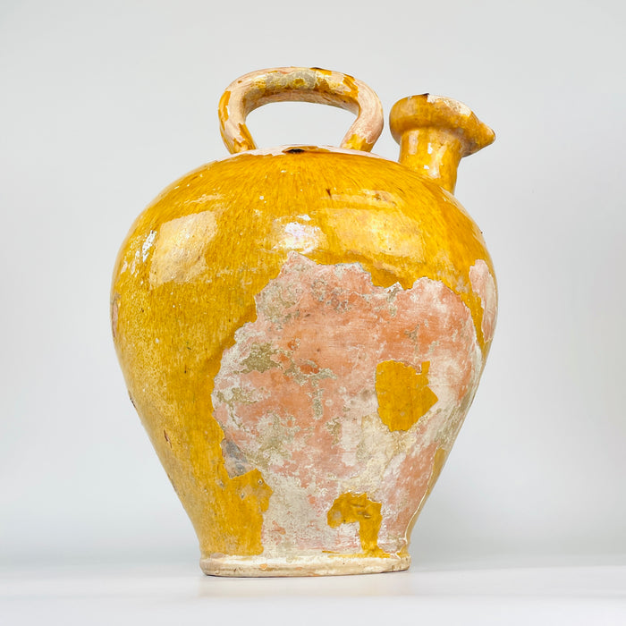 rare French pottery water jug with a large pinched pouring mouth positioned beside a thick overhead handle. The closed terracotta shoulder retains areas of mustard glaze, fine crazing and historic surface wear, distinguishing the vessel from more commonly encountered narrow-necked gargoulettes.