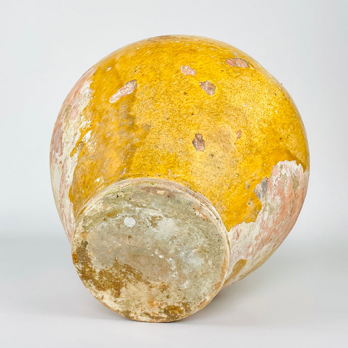 Underside of an antique French cruche showing its flat circular base, narrow foot ring and heavily weathered terracotta surface. Mineral deposits, abrasions and historic glaze loss document prolonged practical use, while the surrounding yellow pottery body confirms traditional Southern French manufacture.