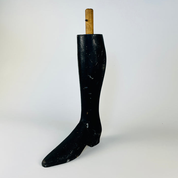 Single antique mannequin leg from France, carved in dense solid wood with a smoothly tapered calf and extended pointed boot. The rubbed black surface reveals warm natural timber at scratches and worn edges, and the round mounting dowel survives above the leg. This graphic Napoleon III object adds a figurative accent to eclectic decor.