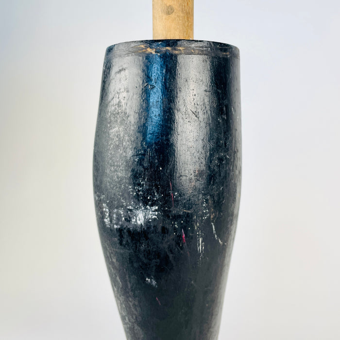 Antique French mannequin leg standing on its carved boot and heel, with the long calf rising to an original wooden mounting dowel and metal retaining pin. The deep black finish is mottled by scratches, rubbed patches and exposed timber from decades of handling. Its period form is especially compatible with Napoleon III decor.