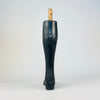 Antique French mannequin leg standing on its carved boot and heel, with the long calf rising to an original wooden mounting dowel and metal retaining pin. The deep black finish is mottled by scratches, rubbed patches and exposed timber from decades of handling. Its period form is especially compatible with Napoleon III decor.