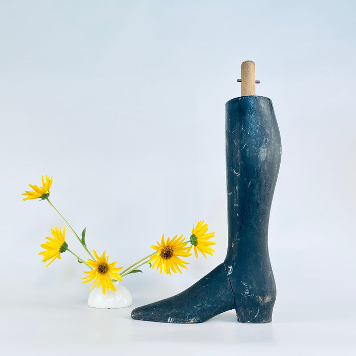 One antique French tailor’s mannequin leg in heavy solid carved wood, held upright to convey its substantial life size scale. The black painted lower leg ends in an elongated pointed boot with a shaped heel, while a pale wooden mounting dowel and transverse metal pin remain at the top. A circa 1870–1890 Napoleon III object suited to oddities decor.