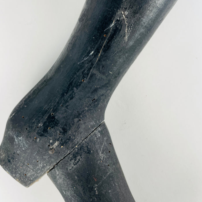 Surface detail of a nineteenth century French tailor’s mannequin leg shows scattered small holes, old scratches, paint abrasion and an open crack through the ankle and heel junction. Pale solid wood is exposed beneath the black painted finish. These condition details remain integral to the antique trade object’s character in dark academia decor.