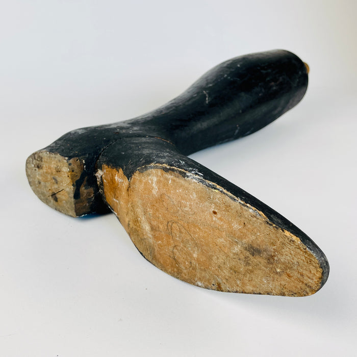 Original attachment hardware on an antique French wooden mannequin leg consists of a pale round dowel rising from the calf and a short metal pin passing through it. The contrast with the worn black painted body makes the former articulated function legible, while the sculptural form offers a strong historical element for fashion studio decor.