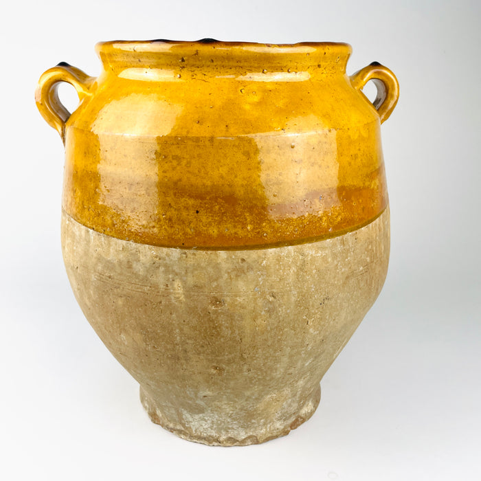 late 19th century French terracotta confit jar with a bulbous body, flared rim and two small ear handles. Honey and ochre glaze covers the shoulder while the lower clay remains matte and weathered, giving this functional food preserving pot strong rustic home decor character.