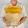 Hand thrown French pottery confit pot with warm ochre glaze ending in an irregular line around the upper body and natural terracotta left exposed below. The contrast between glossy honey color and chalky aged clay defines the traditional preserving jar and complements cottage decor.