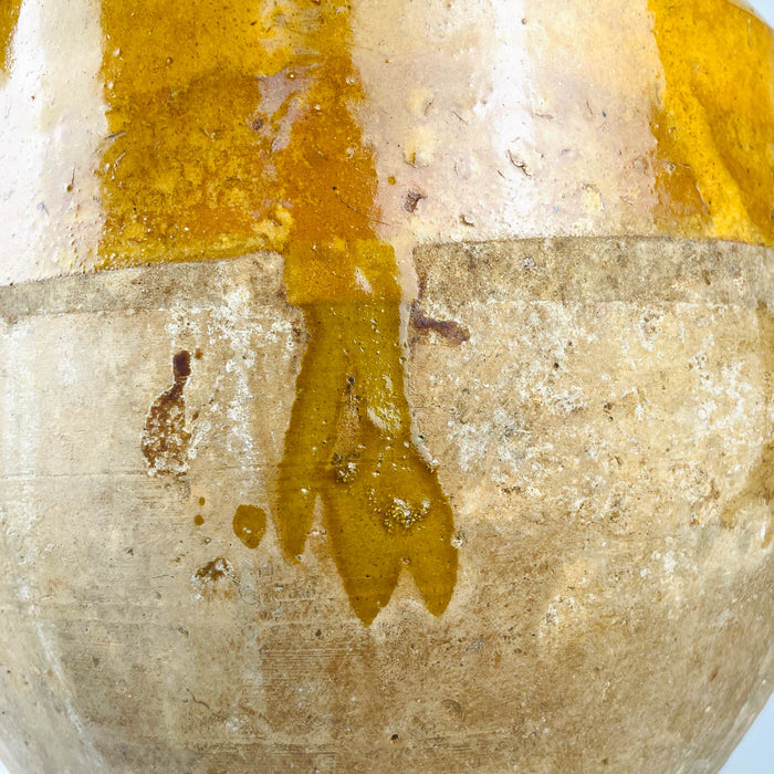 Late 19th century French confit jar in terracotta, with a broad rounded mouth and mustard yellow glaze continuing across the interior. Small chips and glaze losses around the rim expose the clay beneath, while fine crazing and firing speckles record the vessel’s age and handmade provincial pottery character.