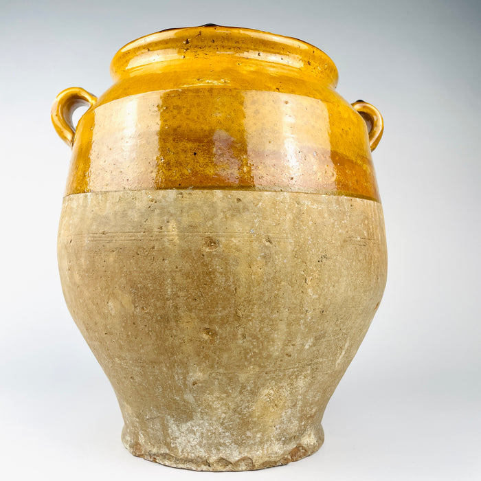Antique French pottery confit pot with a rounded body, paired ear handles and partial ochre glaze, suitable as a decorative cachepot when used with a protective liner. The matte lower terracotta, worn rim and aged glaze give the vessel a strong wabi sabi decor presence.